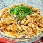 A spicy Chili Crunch Coleslaw with Pineapple is in a glass bowl garnished with sliced green onions.
