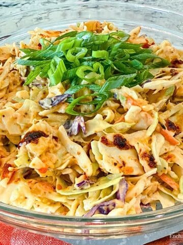 A spicy Chili Crunch Coleslaw with Pineapple is in a glass bowl garnished with sliced green onions.