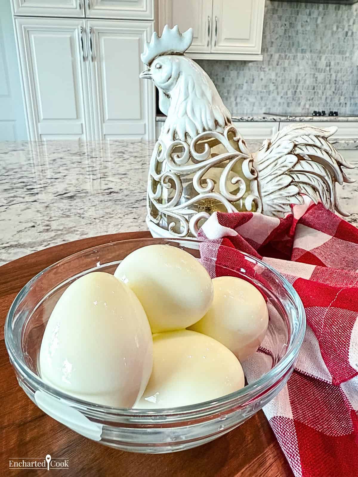 Perfect hard boiled eggs with the eggshell removed and are in a glass bowl with a decorative chicken in the background.