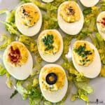 Close up view of Deviled Eggs with various garnishes on a white platter with lettuce.