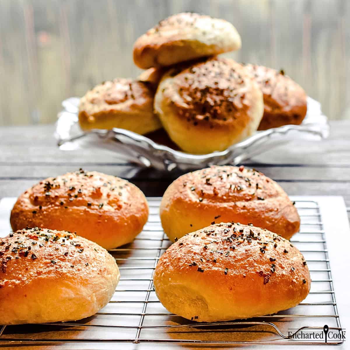 Garlic Parmesan Hamburger Buns on a cooling rack and stacked on a glass plate.