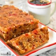 Sliced loaf of No-Bake Biscoff Fruitcake on a platter with a cup of black coffee.