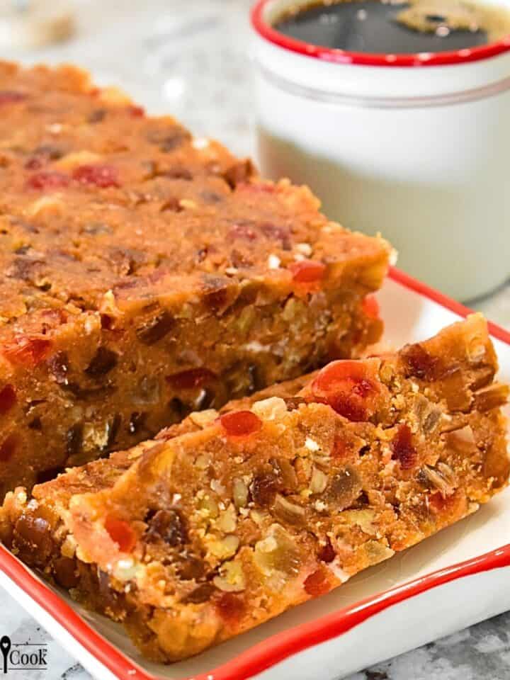 Sliced loaf of No-Bake Biscoff Fruitcake on a platter with a cup of black coffee.