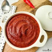 Red Enchilada Sauce in a white dish on a wooden board.