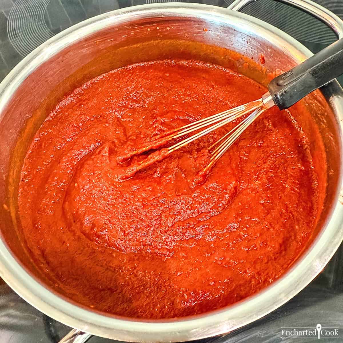 The Red Enchilada Sauce is fully cooked in a sauce pan with a small whisk.