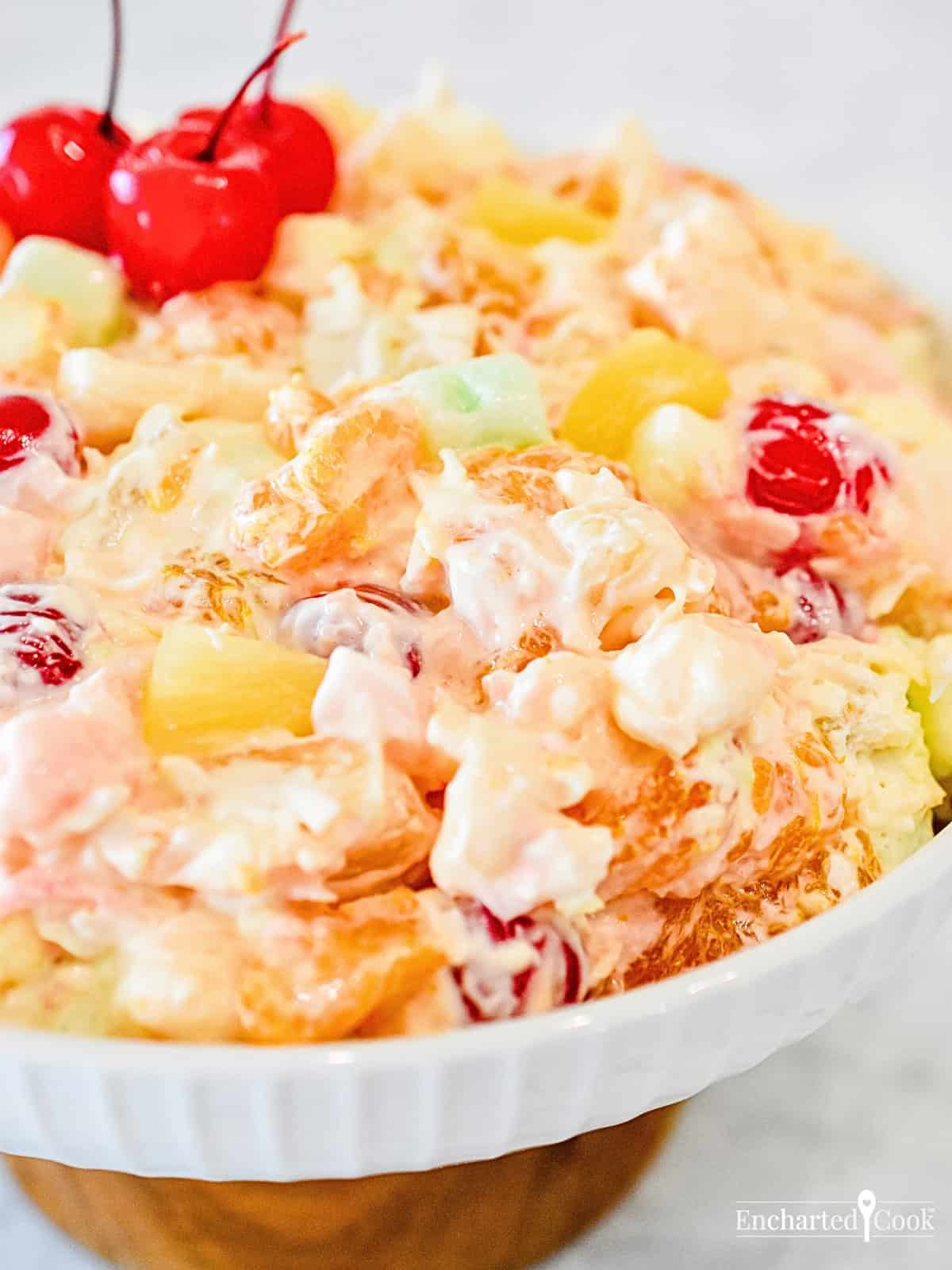 Creamy Traditional Ambrosia Fruit Salad in a white bowl garnished with maraschino cherries.