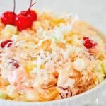 Creamy Traditional Ambrosia Fruit Salad in a white bowl garnished with maraschino cherries.
