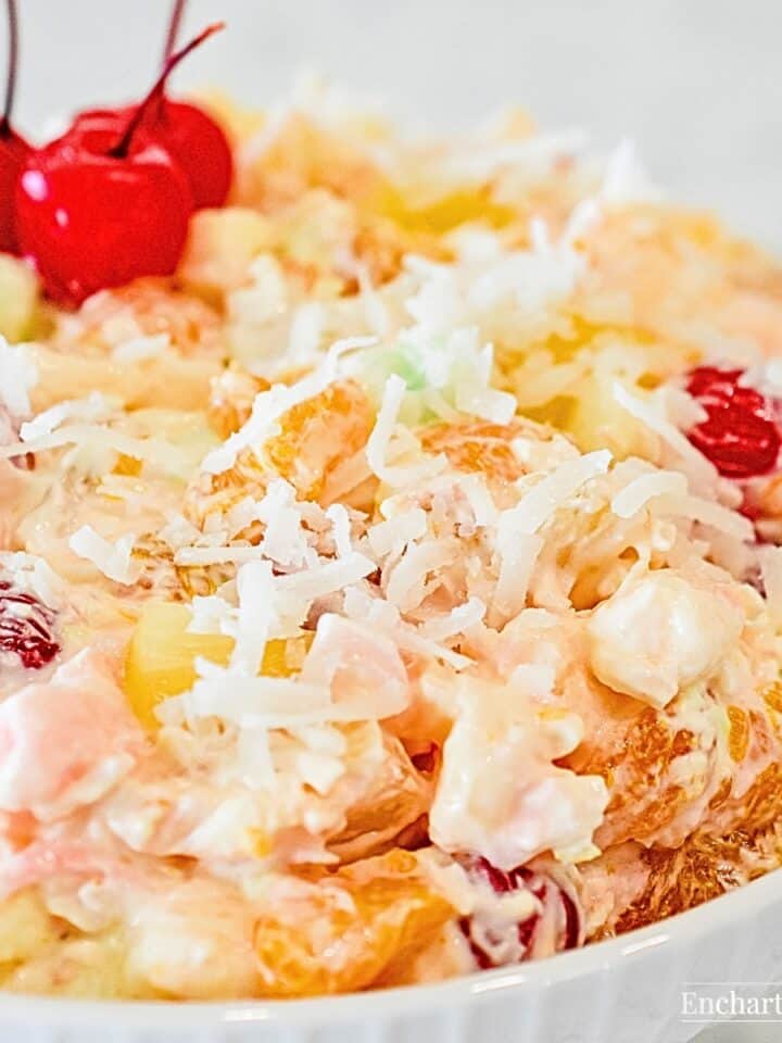 Creamy Traditional Ambrosia Fruit Salad in a white bowl garnished with maraschino cherries.