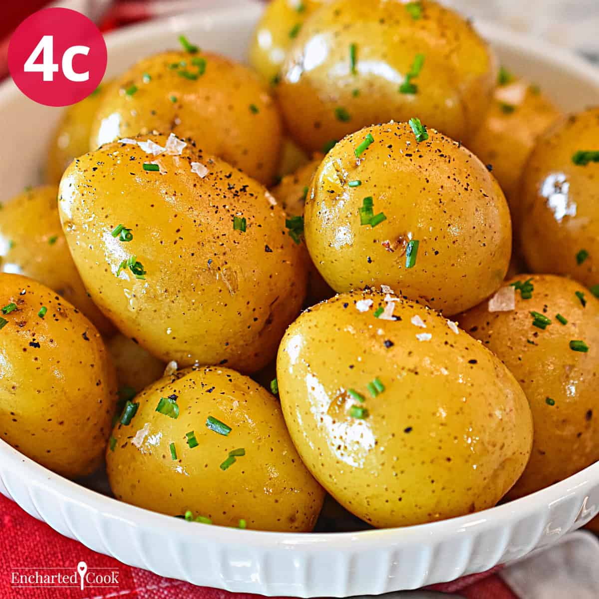 Process Photo 4c - Cooked, hot, small whole potatoes in a white bowl seasoned with black pepper, flakey salt, and chopped green chives.