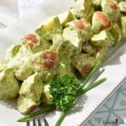 Potato Salad with Green Goddess Dressing on a white platter and garnished with chives and parsley.