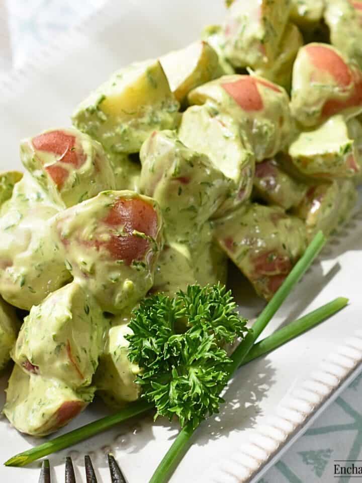 Potato Salad with Green Goddess Dressing on a white platter and garnished with chives and parsley.