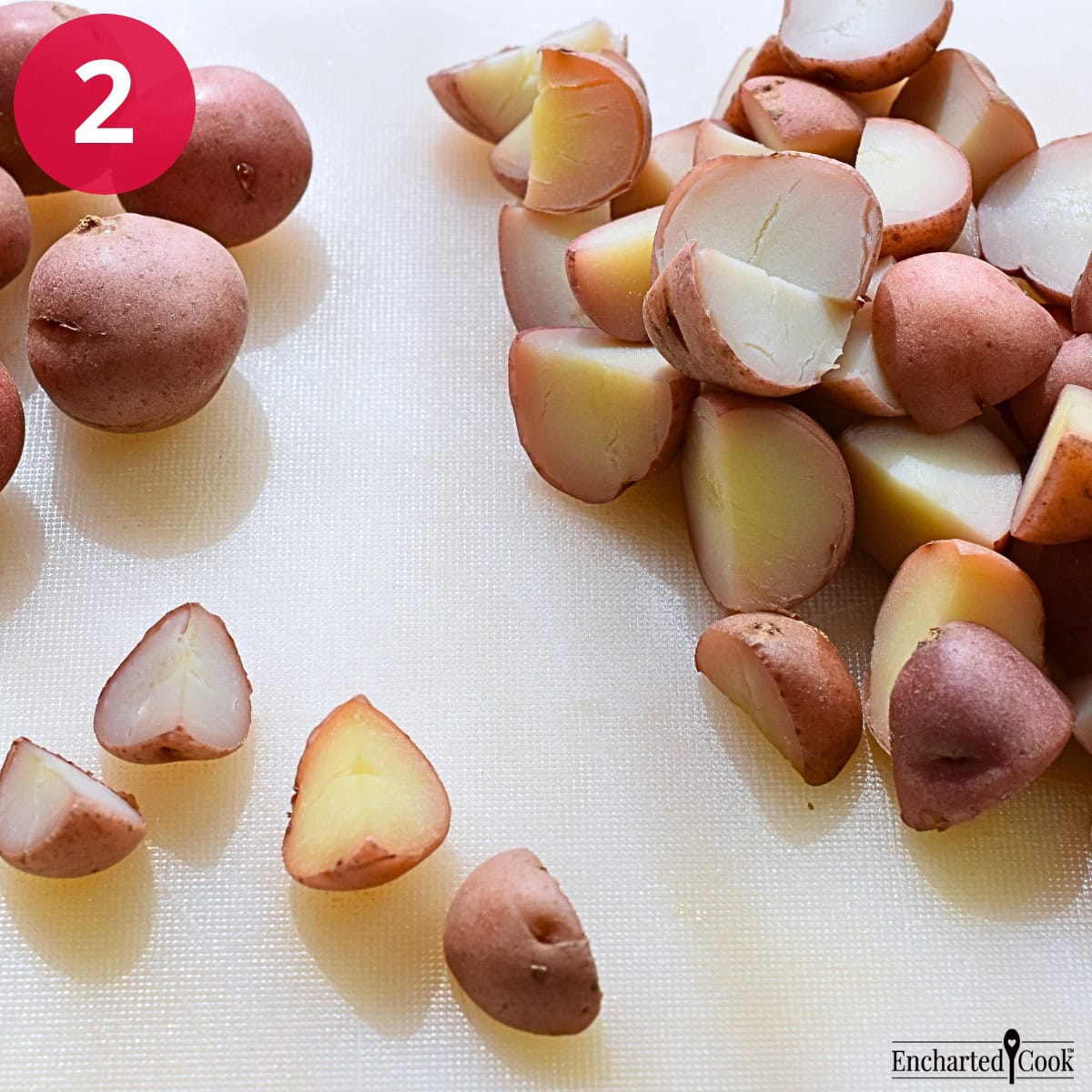 Process Photo 2 - The cooked and cooled red potatoes are cut into bite sized pieces on a white cutting board.