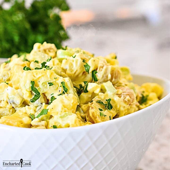 Classic potato salad piled into a white serving bowl.