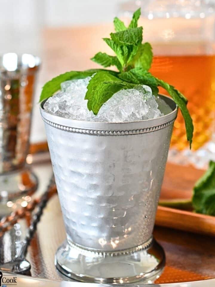 Mint leaves, a decanter of Kentucky bourbon, and a mint julip in a mint julip cup on a silver tray.