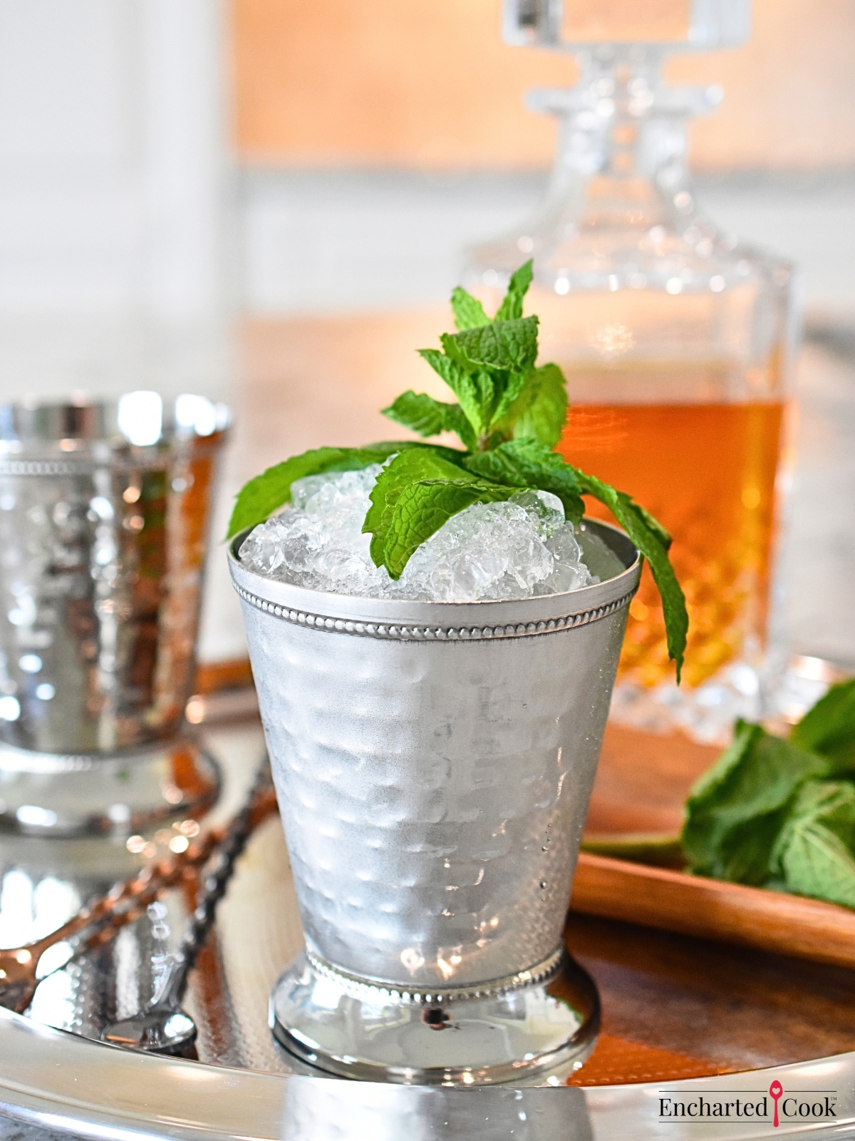 Mint leaves, a decanter of Kentucky bourbon, and a mint julip in a mint julip cup on a silver tray.