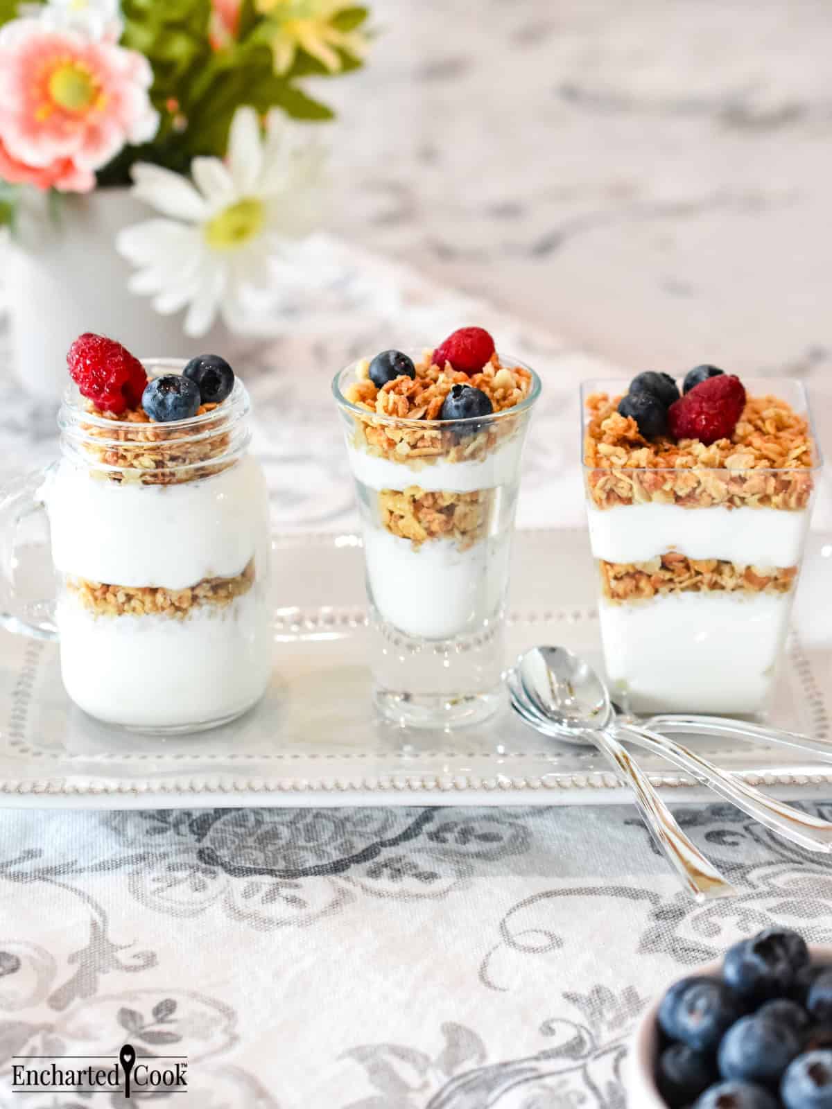 Yogurt Parfait Shooters layered with granola and fruit in a variety glasses, left to right: mini mason jar, large shot glass, and a square dessert cup.