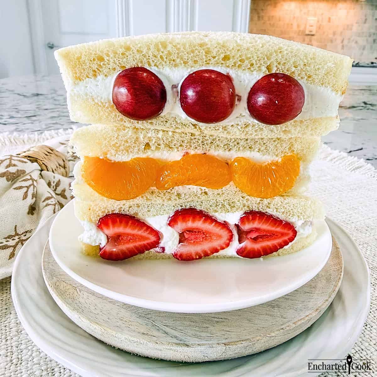 Variations of Fruit Sando on a white plate. From top to bottom: grape, mandarin orange, and strawberry.