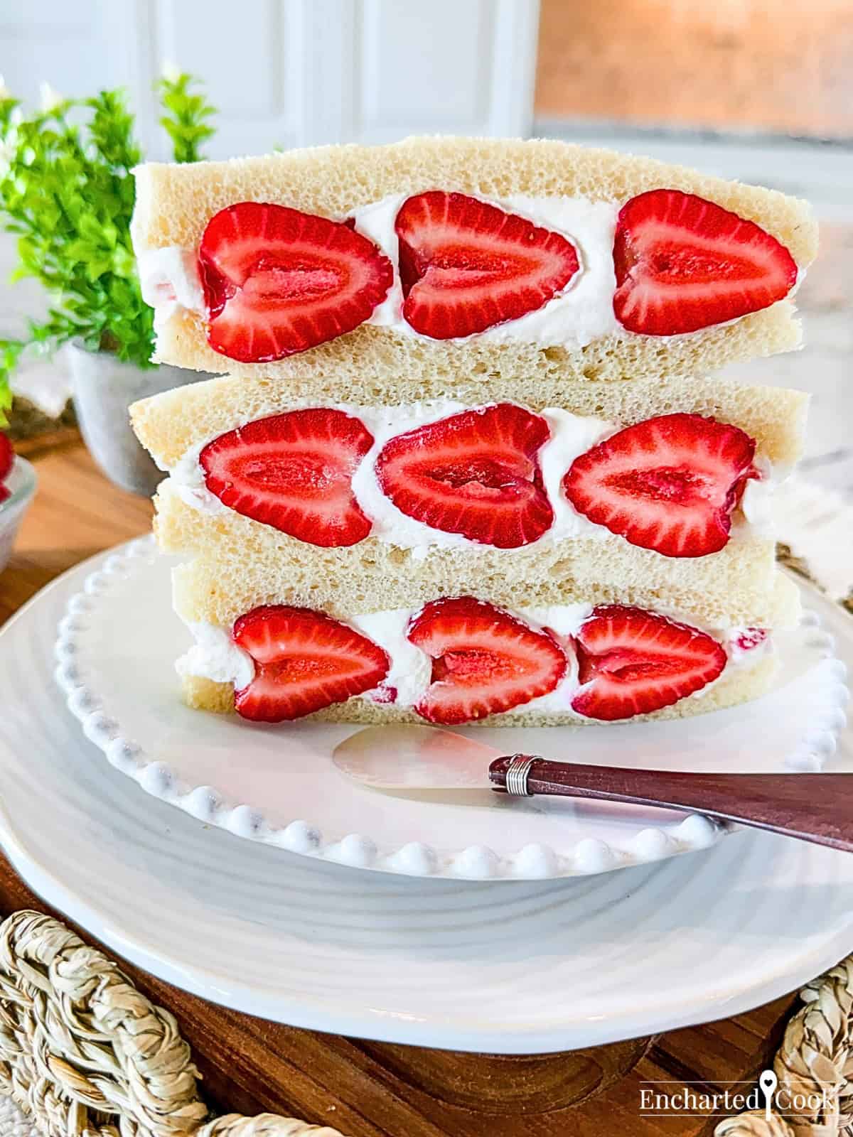 Close view of three Strawberry Sando on a white plate, sitting on a wooden tray with wicker trim.