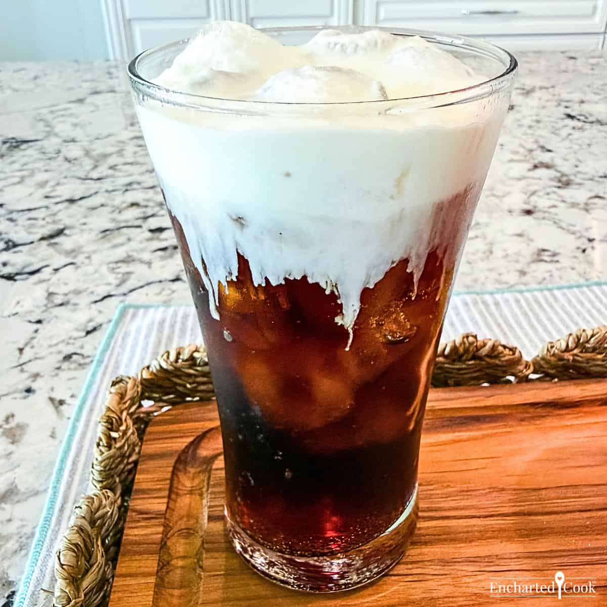 An iced Coca-Cola topped with Vanilla Sweet Cream Cold Foam in a tall glass.