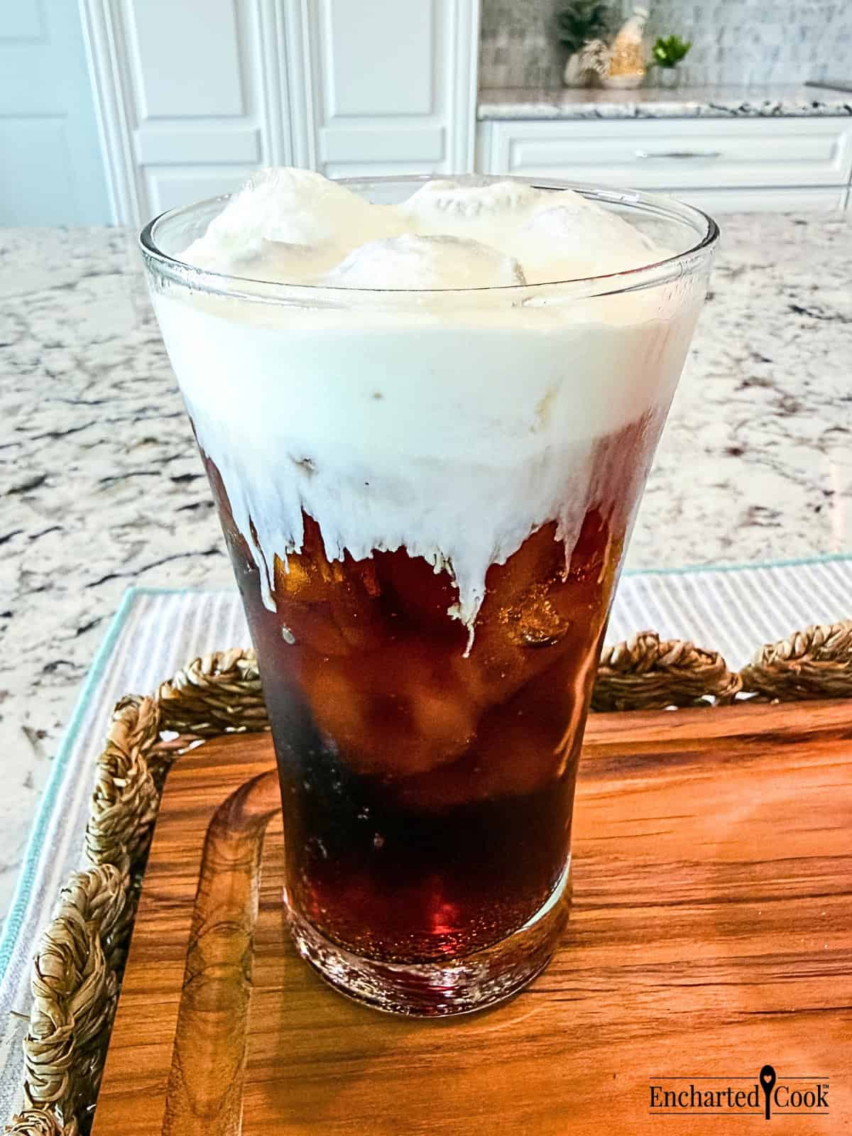 An iced Coca-Cola topped with Vanilla Sweet Cream Cold Foam in a tall glass.