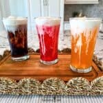 Three iced sodas, cola, fruit punch, and orange, in tall glasses are topped with Vanilla Sweet Cream Cold Foam.