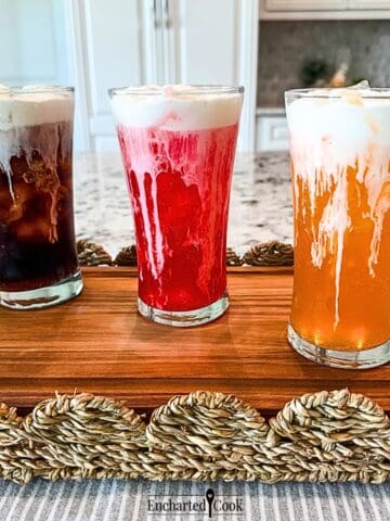 Three iced sodas, cola, fruit punch, and orange, in tall glasses are topped with Vanilla Sweet Cream Cold Foam.