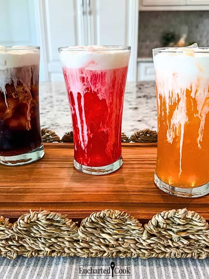 Three iced sodas, cola, fruit punch, and orange, in tall glasses are topped with Vanilla Sweet Cream Cold Foam.