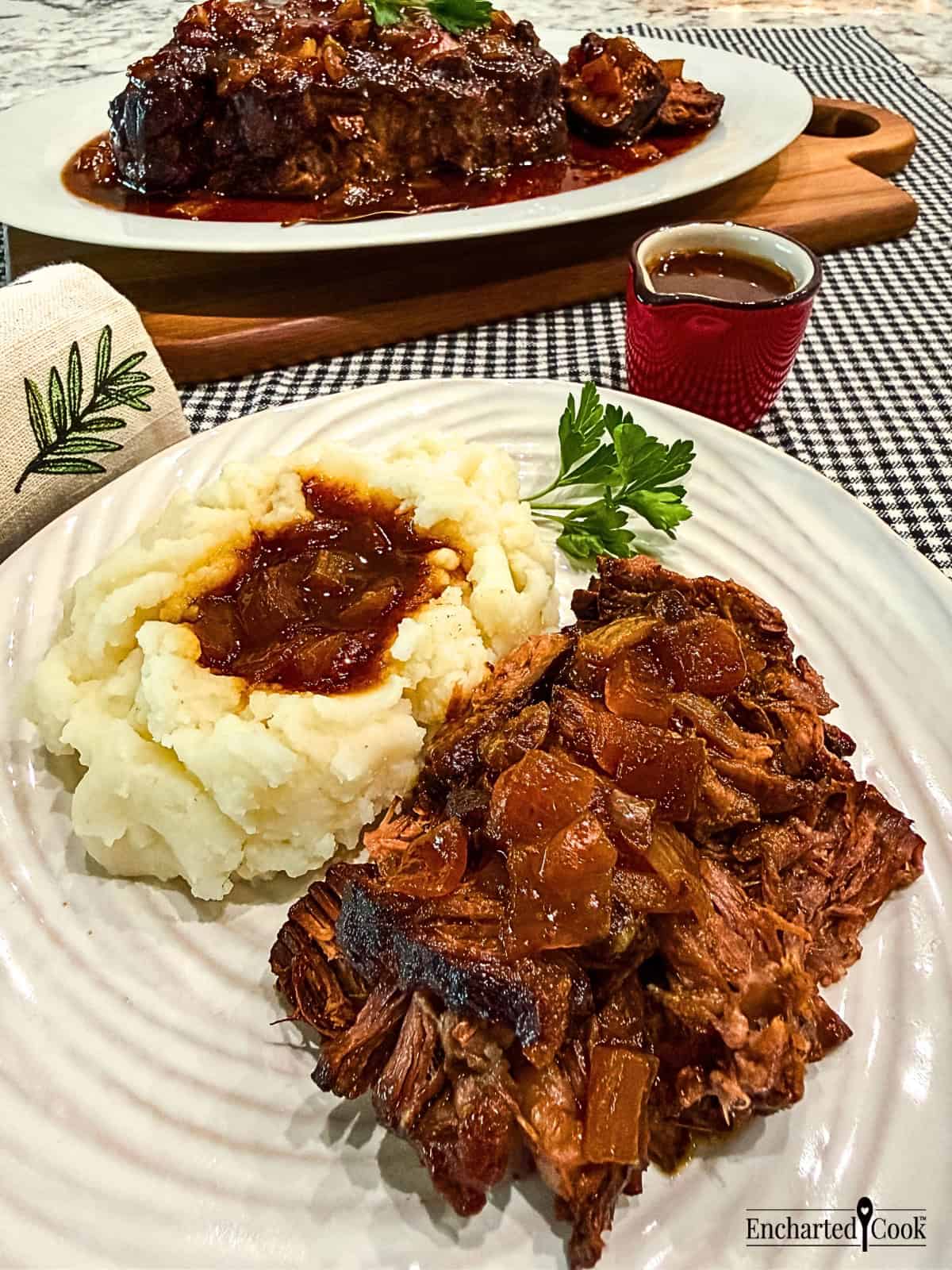 Slow cooker barbecued chuck roast is shredded and served with mashed potatoes and jus poured over the meat and the potatoes.