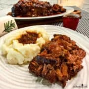 Slow cooker barbecued chuck roast is shredded and served with mashed potatoes and jus poured over the meat and the potatoes.