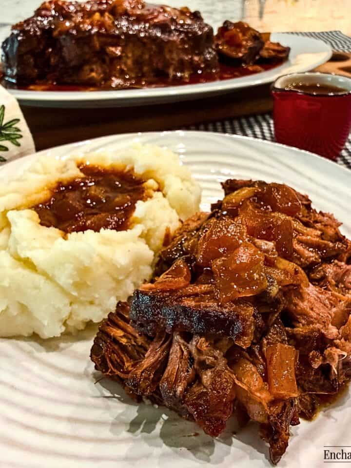 Slow cooker barbecued chuck roast is shredded and served with mashed potatoes and jus poured over the meat and the potatoes.