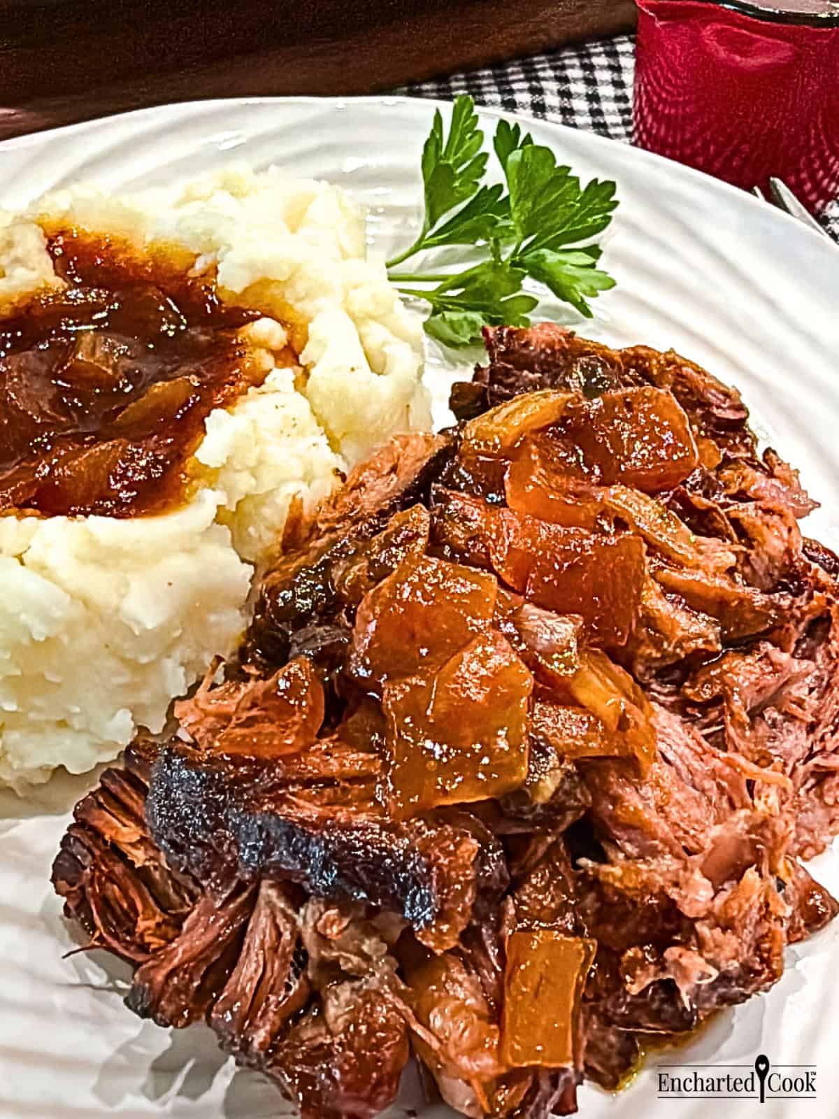 Close up view of slow cooker barbecued chuck roast is shredded and served with mashed potatoes and jus poured over the meat and the potatoes.