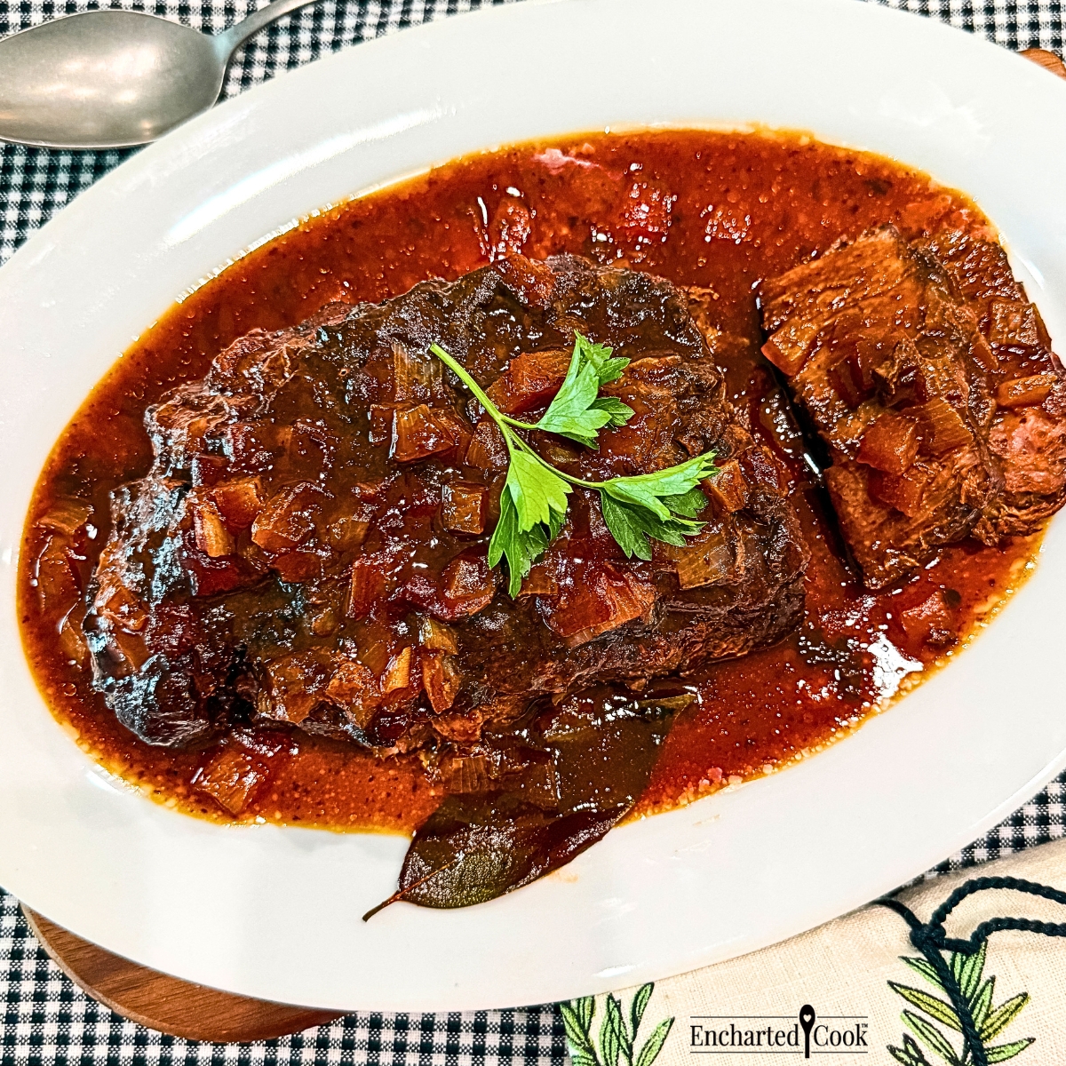 Slow cooker barbecued chuck roast is sliced and jus is poured over the roast and slices on a white platter.
