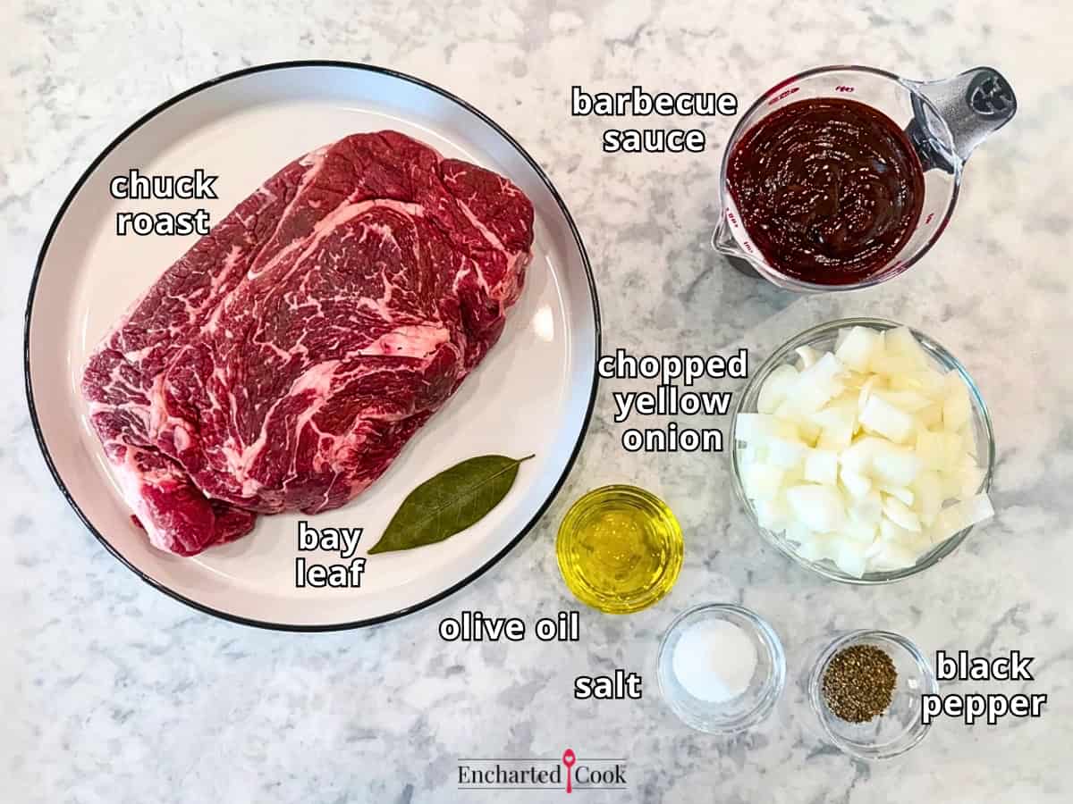 The ingredients, clockwise from top left: chuck roast, barbecue sauce, chopped yellow onion, black pepper, salt, olive oil, and a bay leaf.