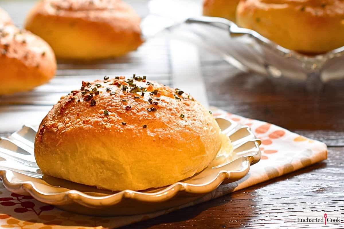 Golden garlic parmesan hamburger bun on a plate with more buns in the background.